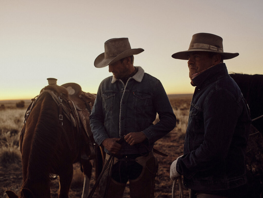 Two cowboys dressed in denim stand next to their horses in an ad campaign for Levi's shot by photographer, Travis Gillet.